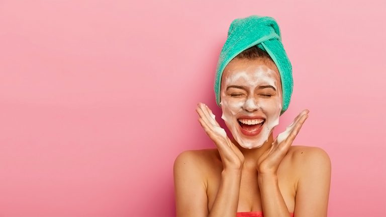 chica sonriendo con una mascarilla de belleza en la cara y una toalla en el pelo